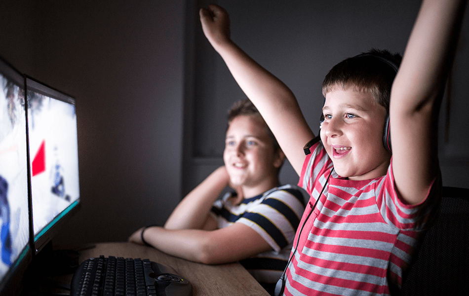 Two excited kids, one raising their arm in joy, as they look at a computer screen