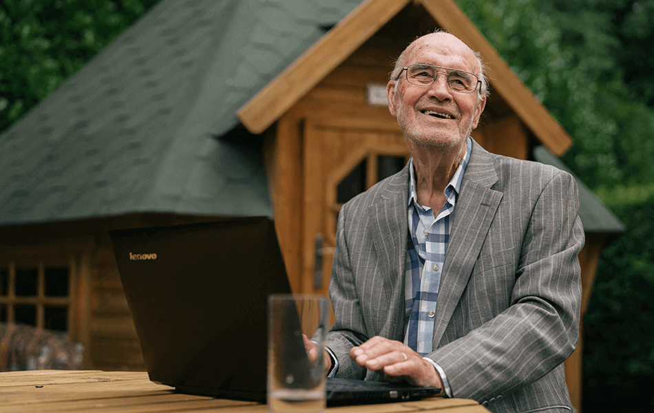 Malcom in the garden on his laptop. His shed is behind him. He's looking away smiling.